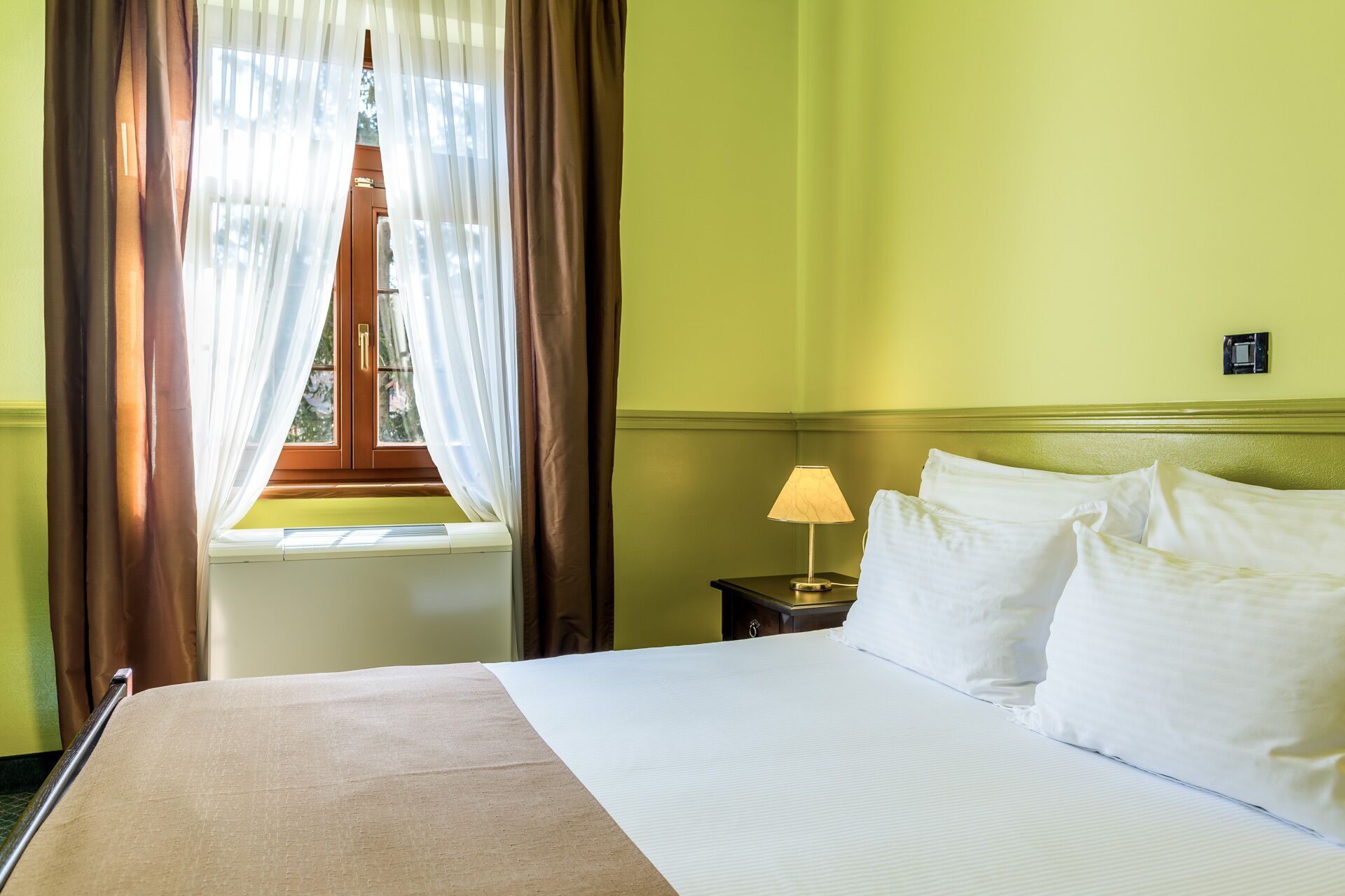 A hotel room with a bed, a nightstand with a lamp, and a window with curtains.