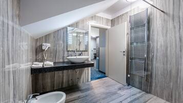 A modern bathroom with a black countertop sink, a white basin, and a bidet. The walls have a wood-like texture, and there's a mirror above the sink.