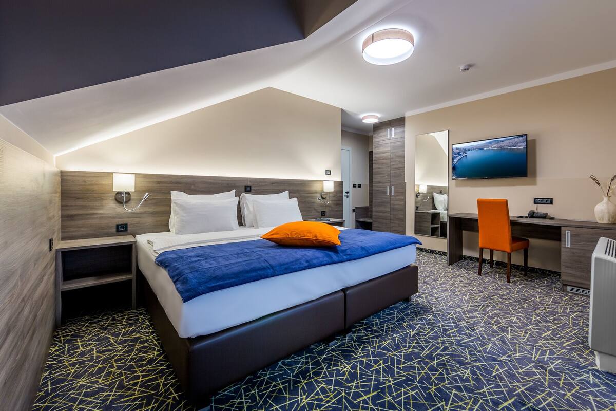 A modern hotel room with a large bed, a desk, a chair, a TV, and a bathroom.