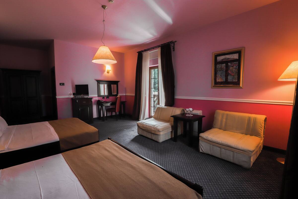 A hotel room with two beds, a desk, a chair, a sofa, and a small table.