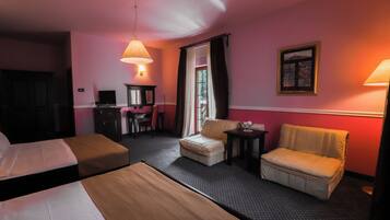 A hotel room with two beds, a desk, a chair, a sofa, and a small table.