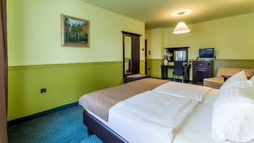 Una habitación de hotel con cama, escritorio, silla, espejo y un cuadro en la pared.