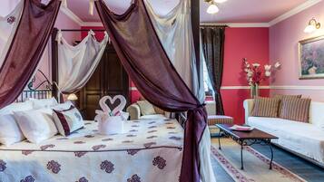 A four-poster canopy bed with a floral bedspread, a bedside table with a vase of flowers, and a sofa with striped cushions.
