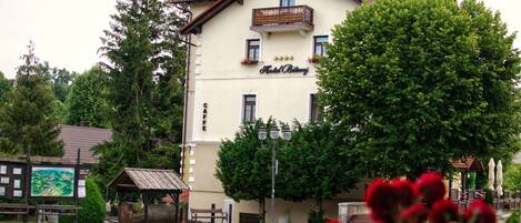 A hotel with a balcony, a sign reading "Hotel Bitomi", and a view of a street with a bench and a wooden structure.
