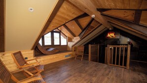 Una habitación acogedora en el ático, con techo inclinado, vigas de madera, un banco empotrado y chimenea.