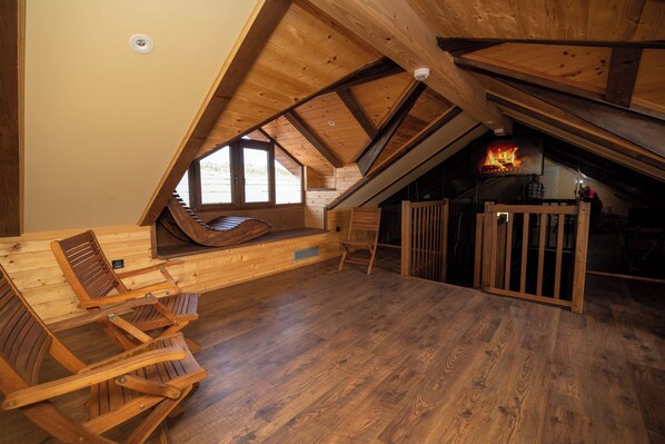 A cozy attic room with a sloped ceiling, wooden beams, a built-in bench, and a fireplace.