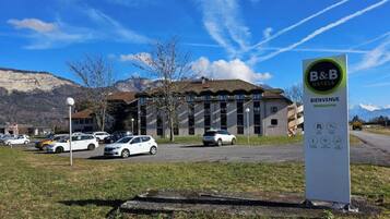 A B&B hotel with a signboard, parking area, and a mountainous backdrop.