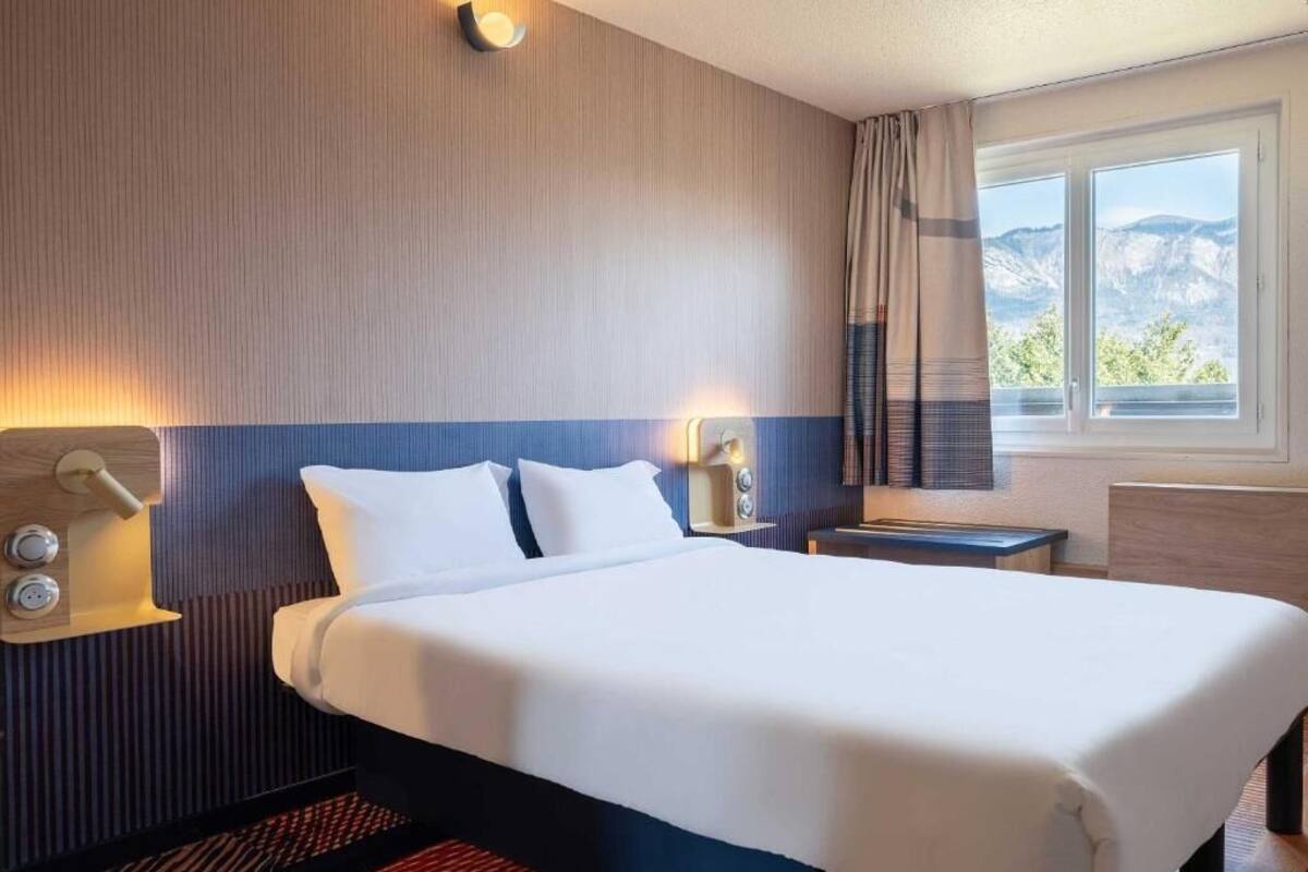 Habitación de hotel con una cama grande, dos mesitas de noche y una ventana con vista a la montaña.