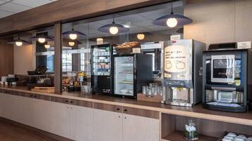 Un área de desayuno autoservicio con refrigeradores, una cafetera y un dispensador de bebidas.