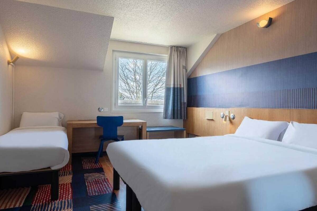 Habitación de hotel con dos camas, un escritorio, una silla y ventana con vista a árboles.