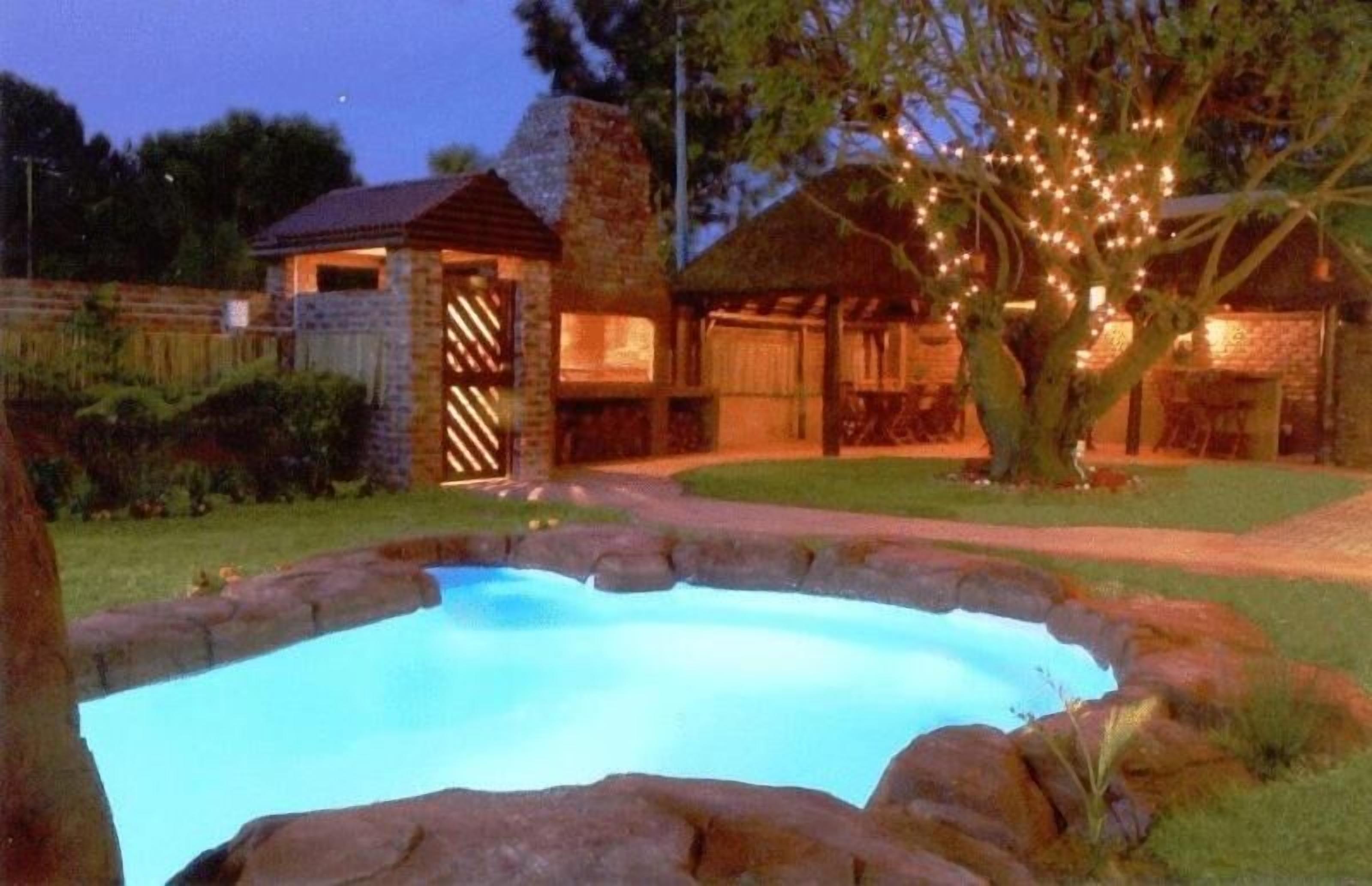 Una piscina rodeada de muros de piedra, una terraza de madera y un árbol con luces colgantes.