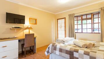 Una habitación de hotel con cama, escritorio, silla, televisor y ventana con cortinas.