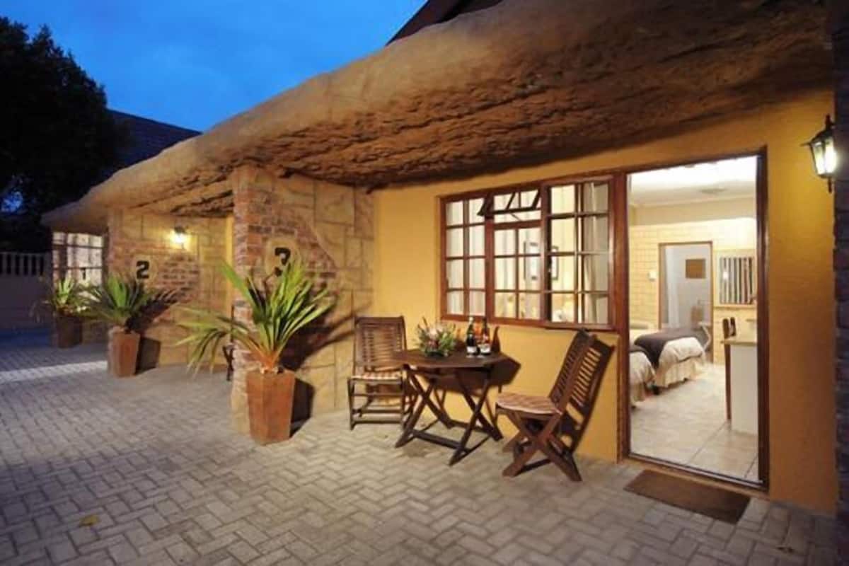 A rustic building with a thatched roof, a brick exterior, and a wooden table and chairs outside.