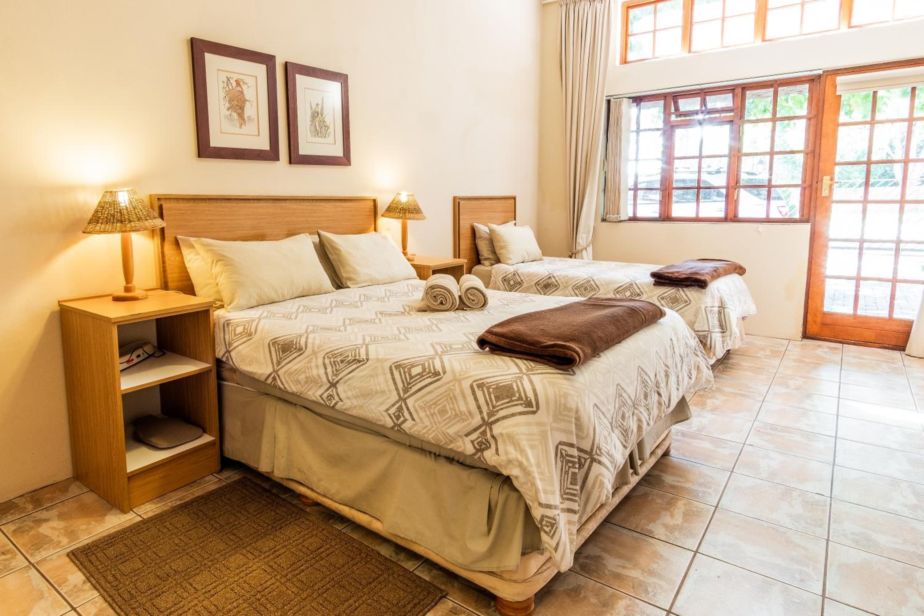 Habitación de hotel con dos camas, una mesita de noche de madera, un estante y una ventana con cortinas.