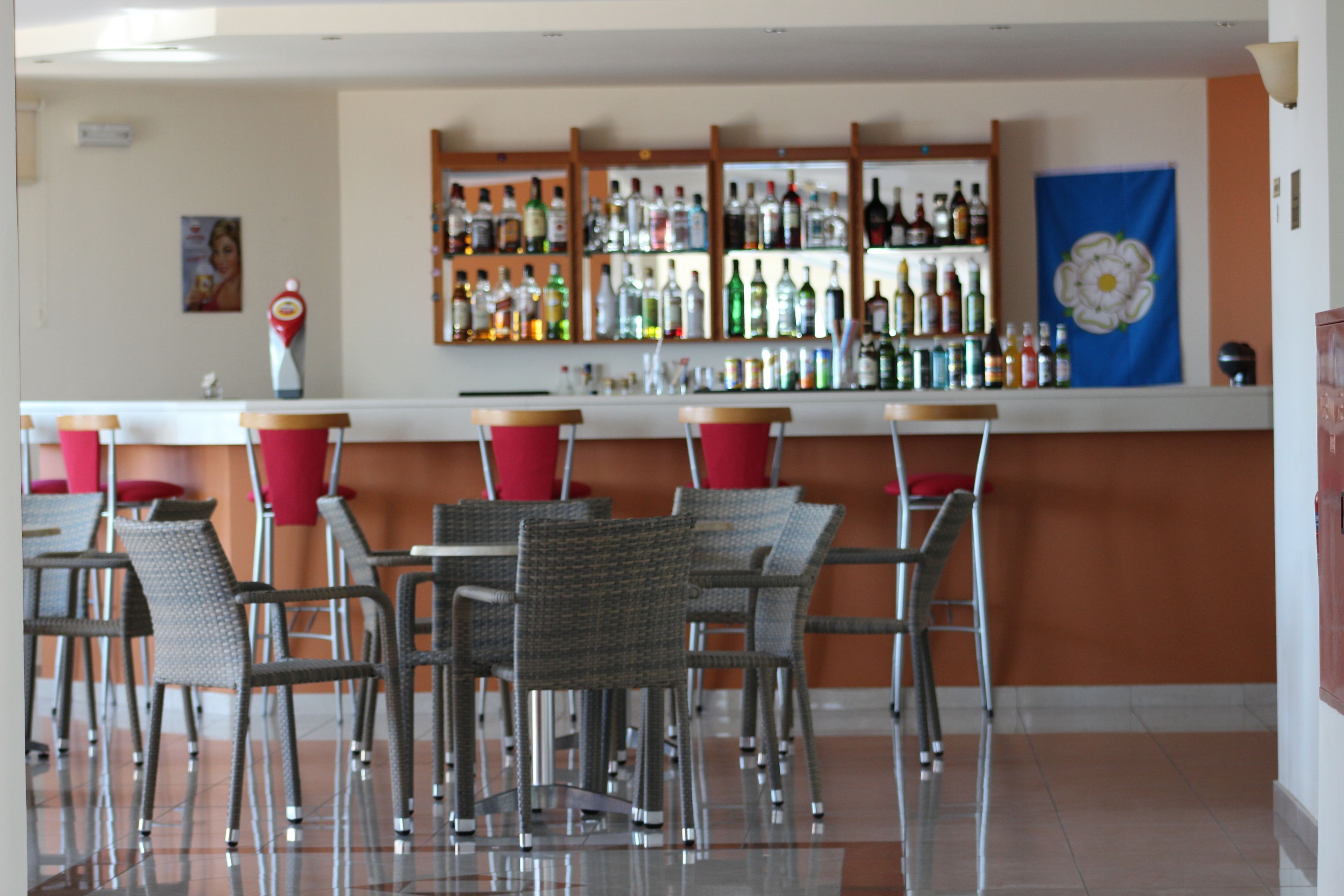 Zona de bar con sillas de mimbre y un mostrador que exhibe diversas botellas.