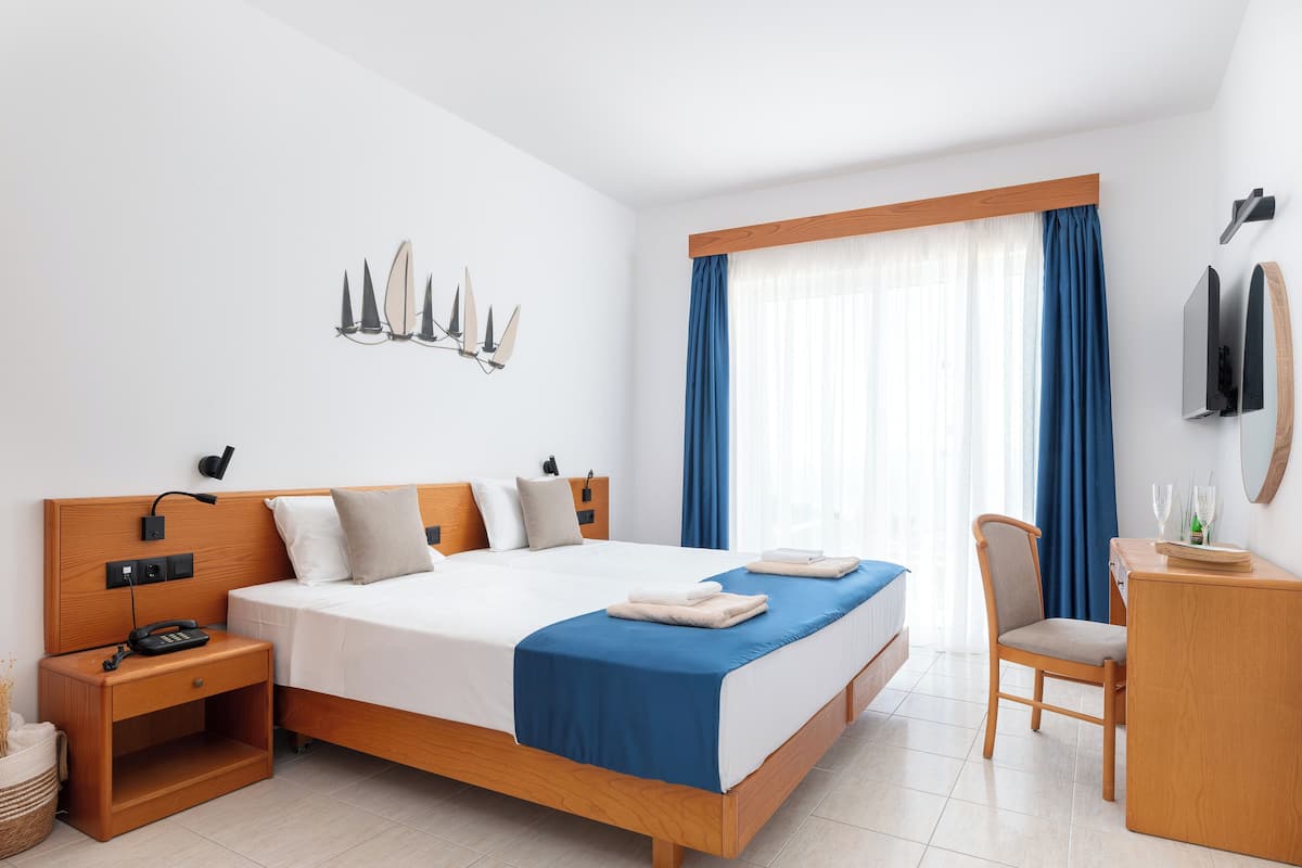 A modern hotel room with a large bed, bedside table, chair, and a TV mounted on the wall.