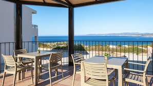 A terrace with a table and chairs, a view of the sea, and a building in the background. - Lindos Nest (Rhodes)