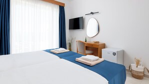 A hotel room with a large bed, a desk, a television, and a small refrigerator. - Lindos Nest (Rhodes)