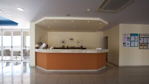 A reception area with a curved counter, framed pictures on the wall, and a bulletin board with travel information. - Lindos Nest (Rhodes)