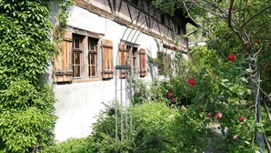 Un edificio tradicional con contraventanas de madera, rodeado de exuberante vegetación y plantas con flores.