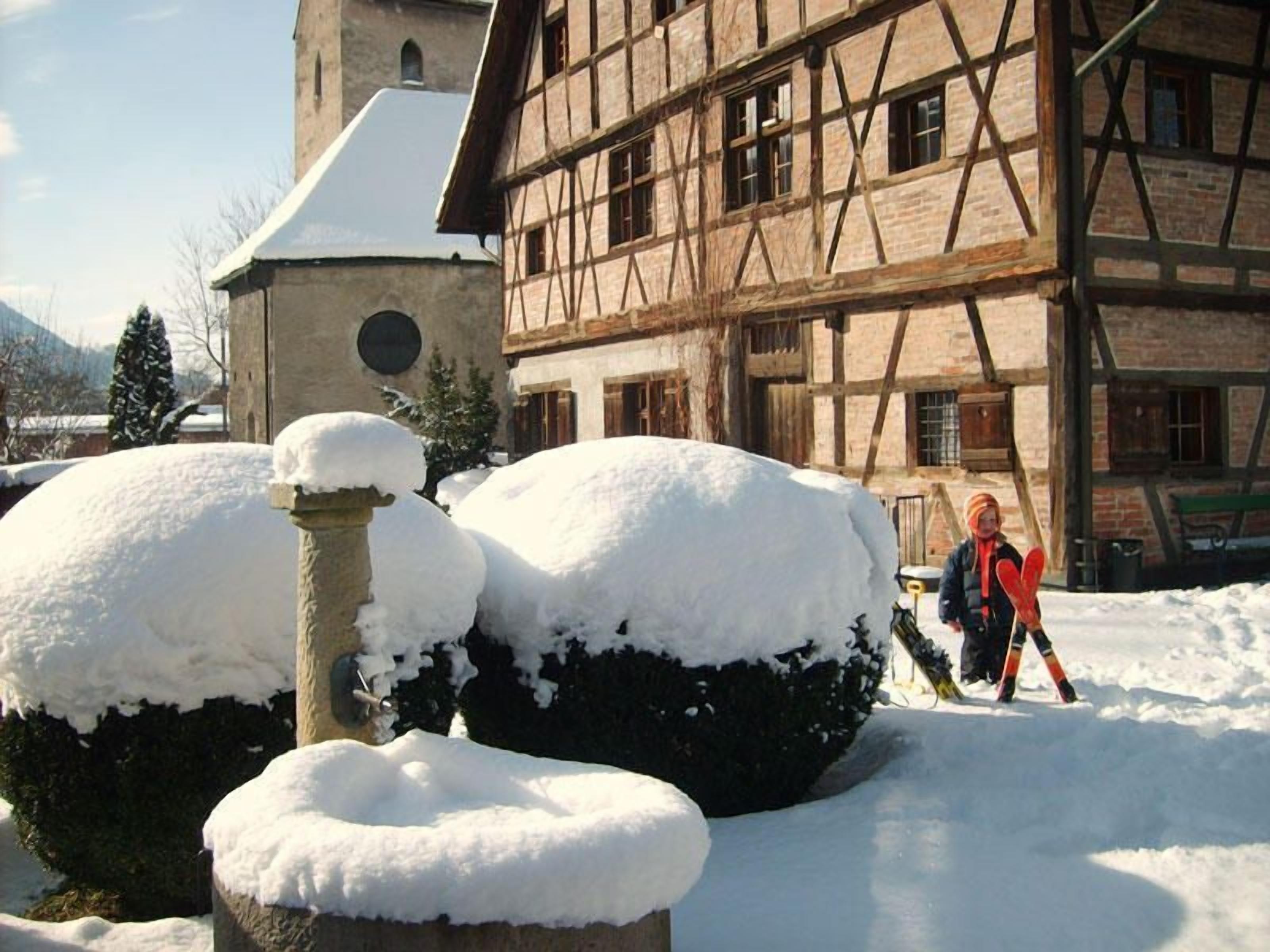 Un edificio tradicional de entramado de madera con arbustos cubiertos de nieve al frente.