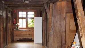 Interior de una cabaña de madera con suelo de madera, un refrigerador blanco, un banco de madera y una ventana con vistas a la vegetación.