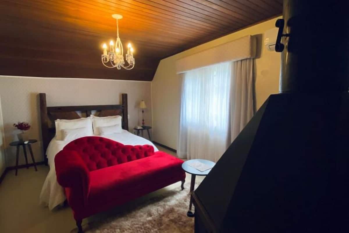 A bedroom with a large bed, a chandelier, a small table, and a window with curtains.