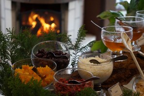 A table with various food items and a glass of tea, set against a background with a fireplace.