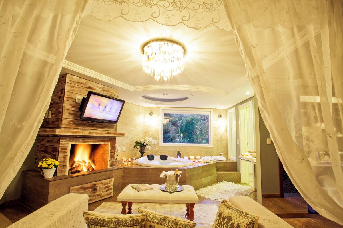 A luxurious room with a fireplace, a large window, a bathtub, and a television.