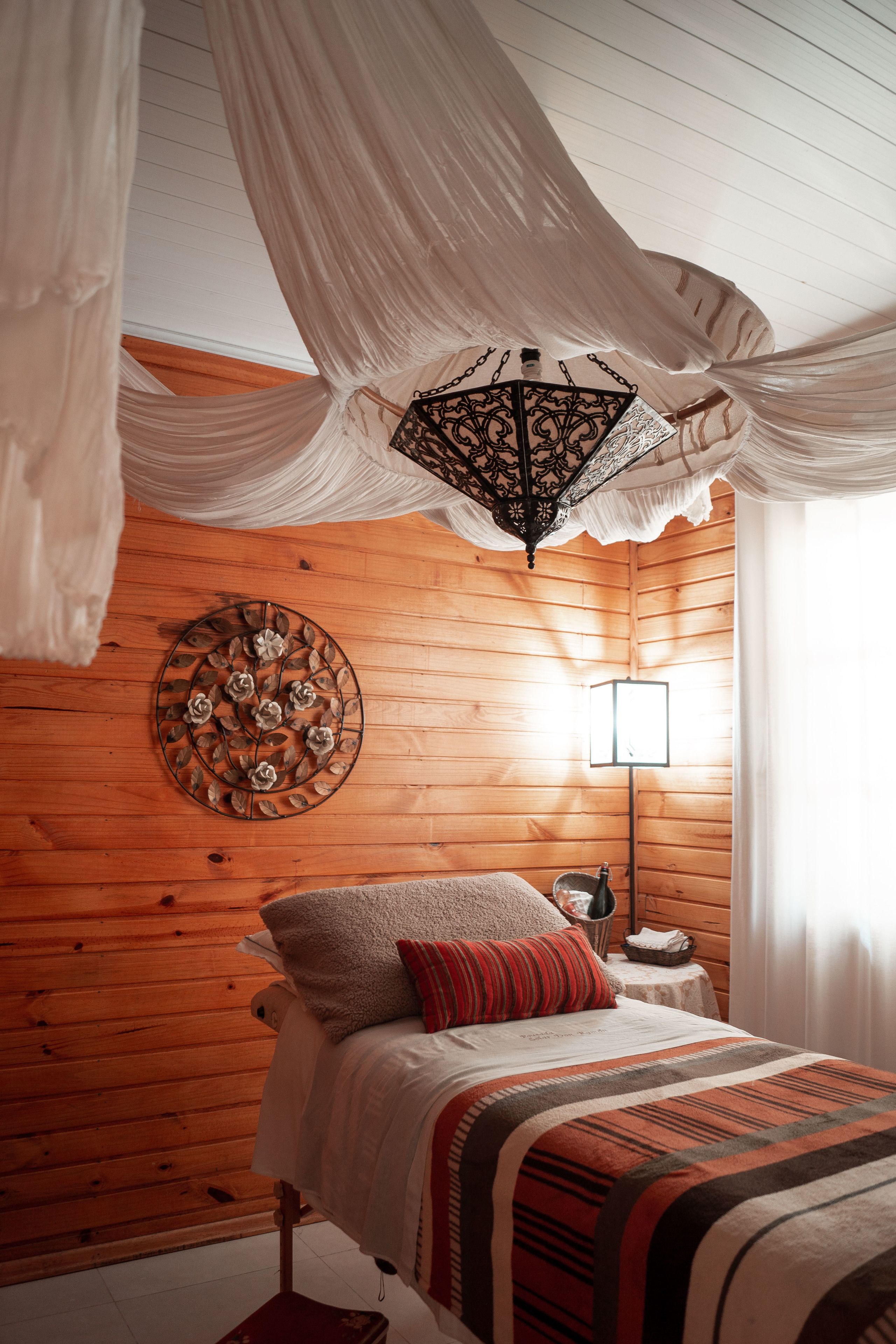 A bedroom with a wooden wall, a bed with a striped blanket, a decorative wall piece, and a hanging light fixture.