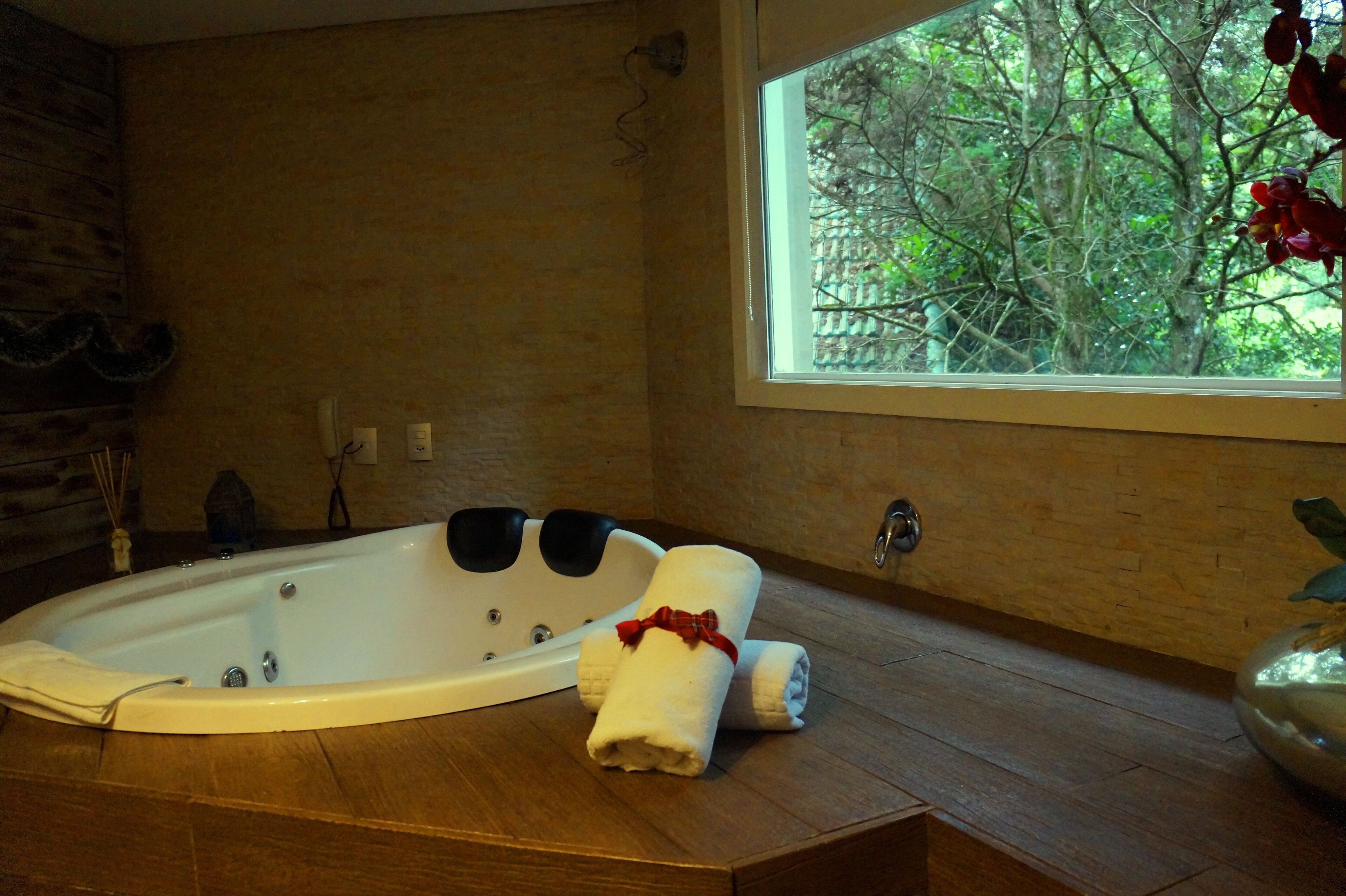 A bathroom with a large bathtub, a window with a view of trees, and a wooden floor.