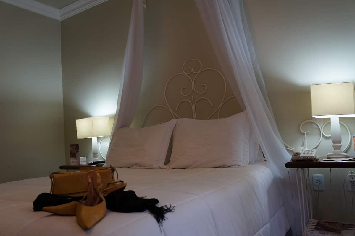 A bed with a canopy, bedside lamps, a bedside table with a phone, and a handbag on the bed.