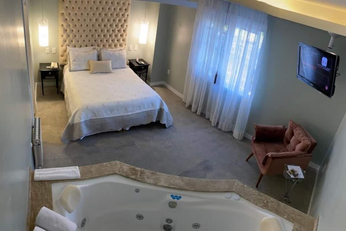 A hotel room with a large bed, a sitting area with a chair, a TV mounted on the wall, and a bathtub.