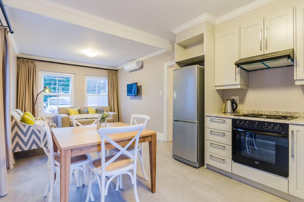 Een moderne keuken met een koelkast, oven en magnetron. Er is een eethoek met een tafel en stoelen.