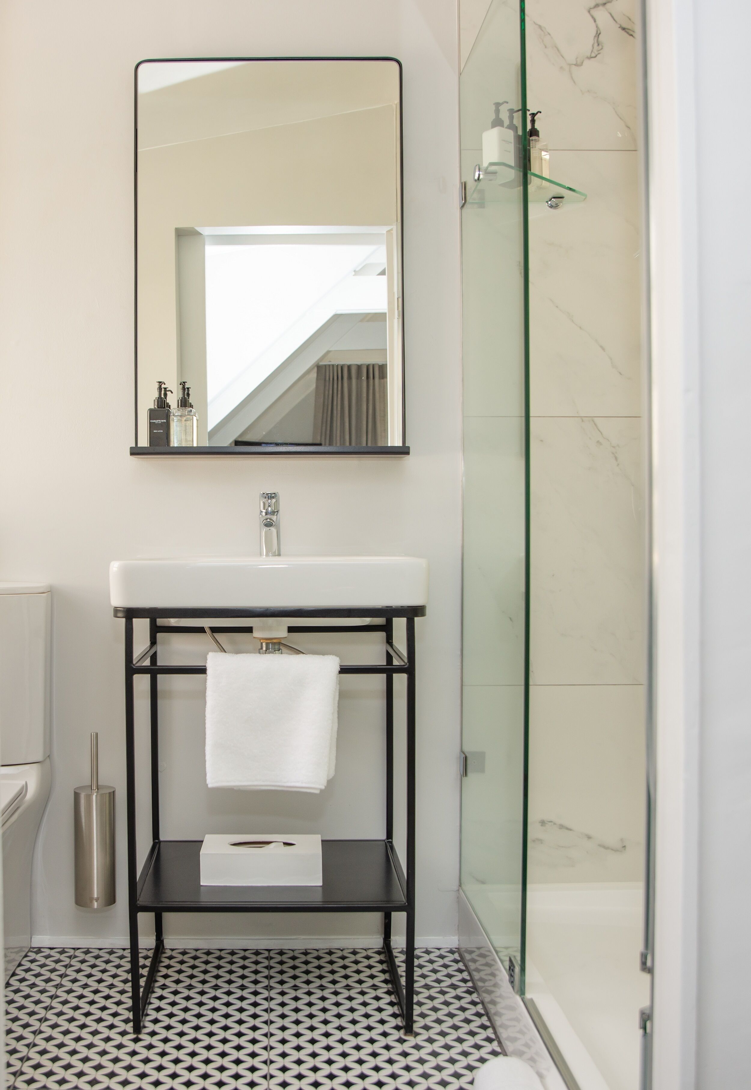 A bathroom with a white sink, a mirror, a glass shower enclosure, and a patterned floor.