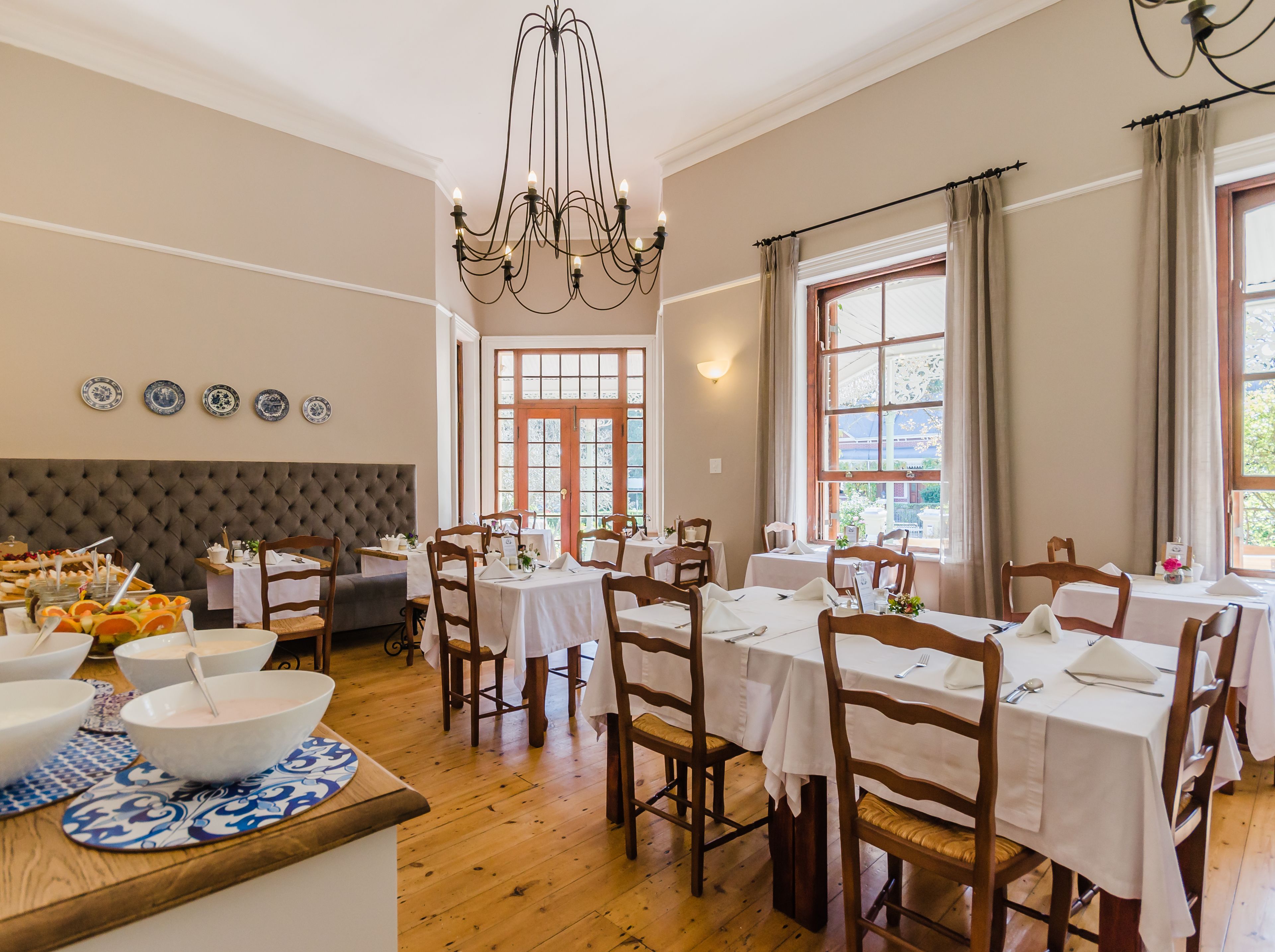 A dining area with multiple tables and chairs, a chandelier, and a large window with curtains.