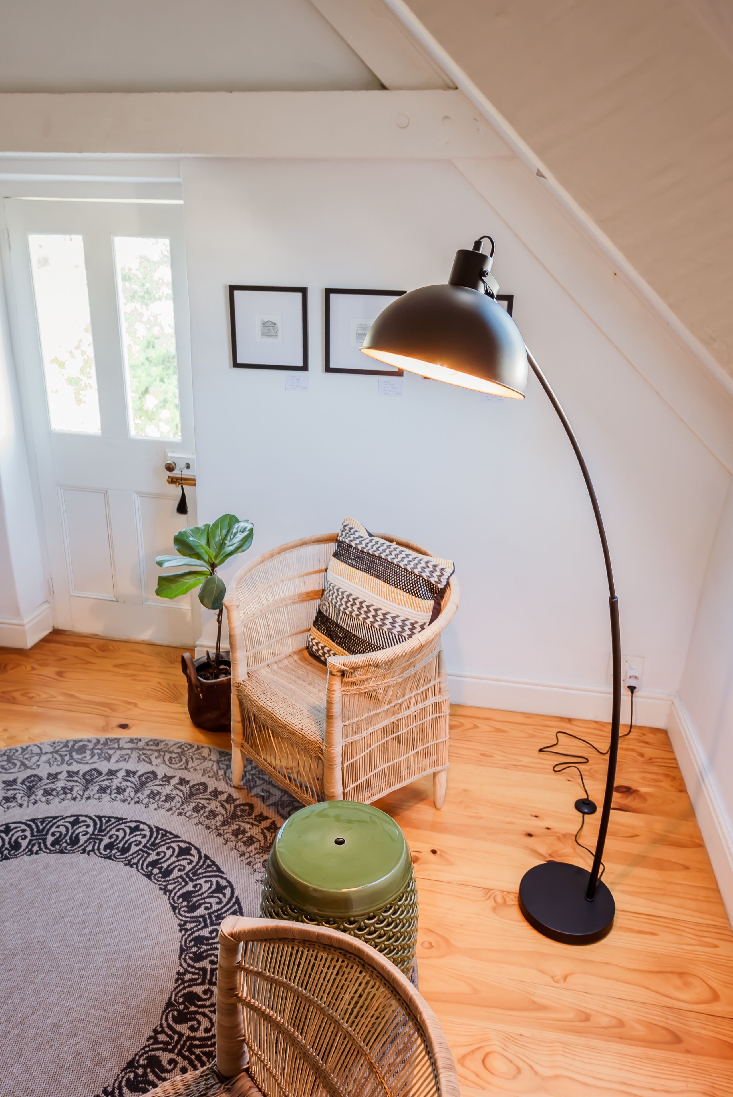 A cozy room with a wicker chair, a floor lamp, and a green stool.