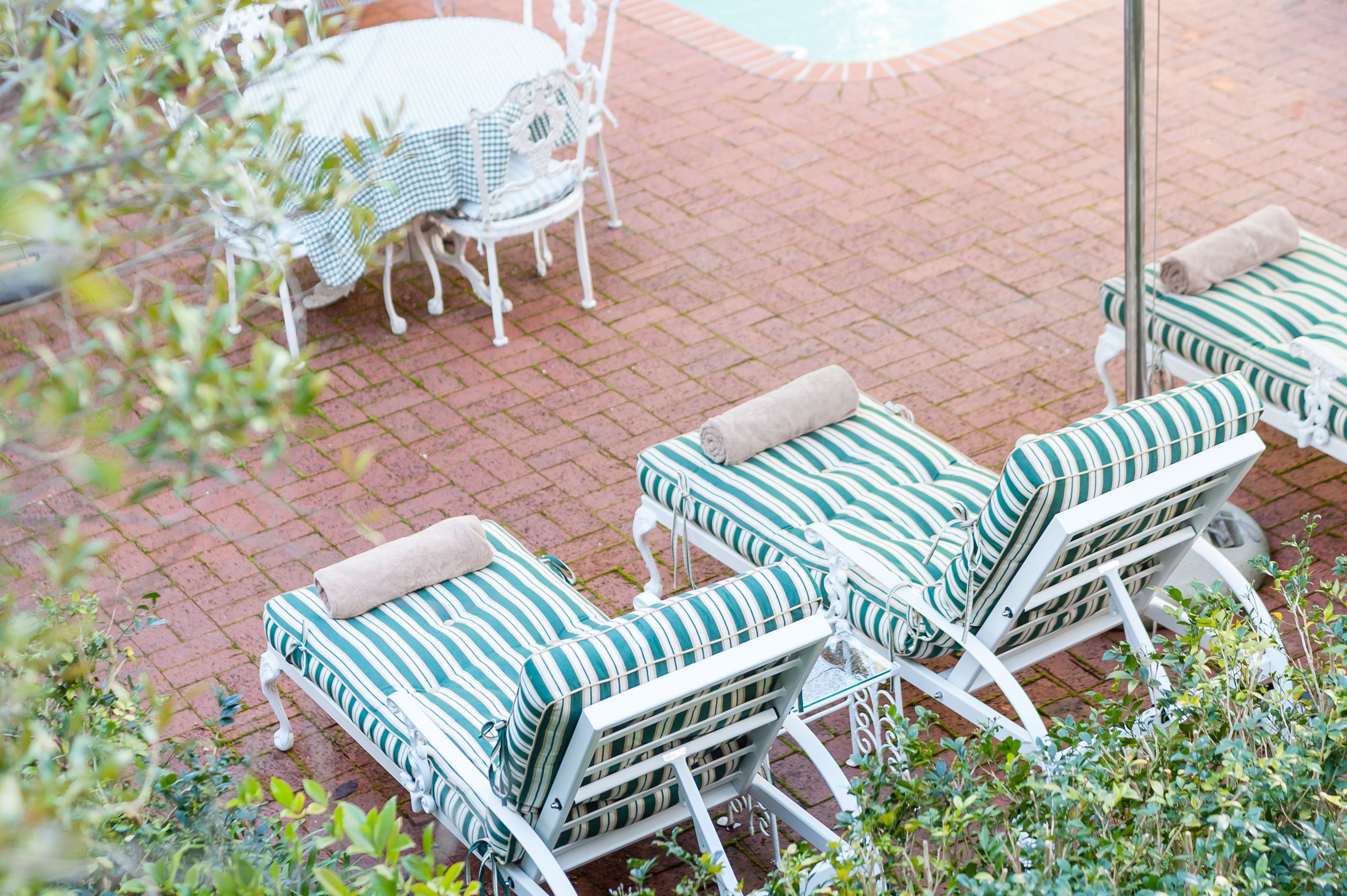 Outdoor seating with striped cushions and white metal frames, a round table with a checkered tablecloth, and a brick patio.