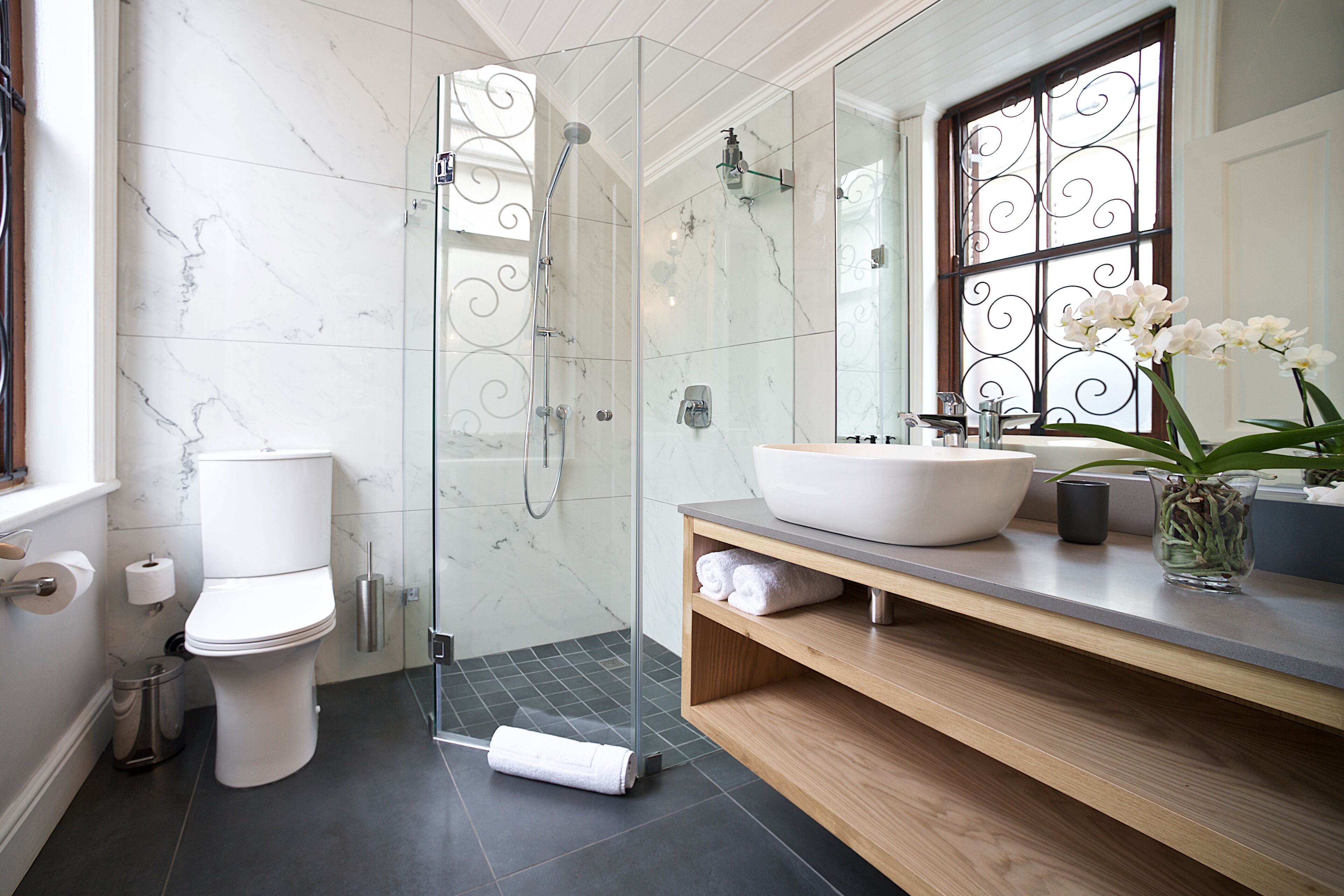 Un baño moderno con ducha de vidrio, inodoro blanco, lavamanos grande y espejo con un vano decorativo.