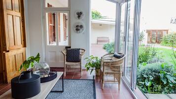 Una habitación iluminada por el sol con puerta de madera, sillas de mimbre, puerta de cristal que da al exterior y una planta en maceta.