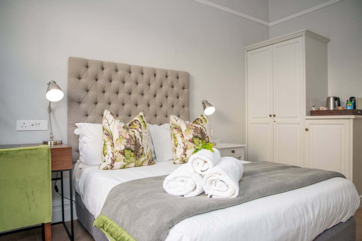Een net opgemaakt bed met opgerolde handdoeken, een gebobbelde hoofdbord, bloemenkussens en bedlampjes.