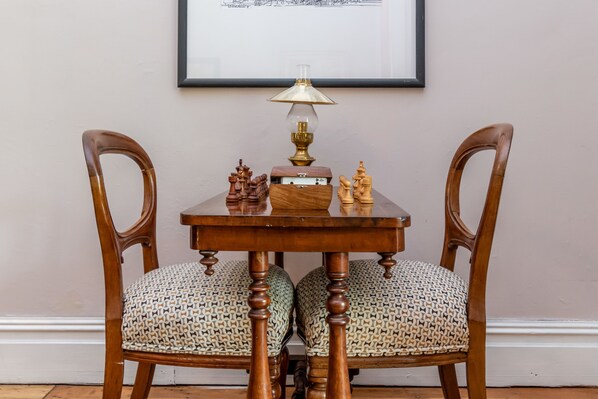 A wooden table with a chess set and a lamp, flanked by two upholstered chairs with a woven pattern.