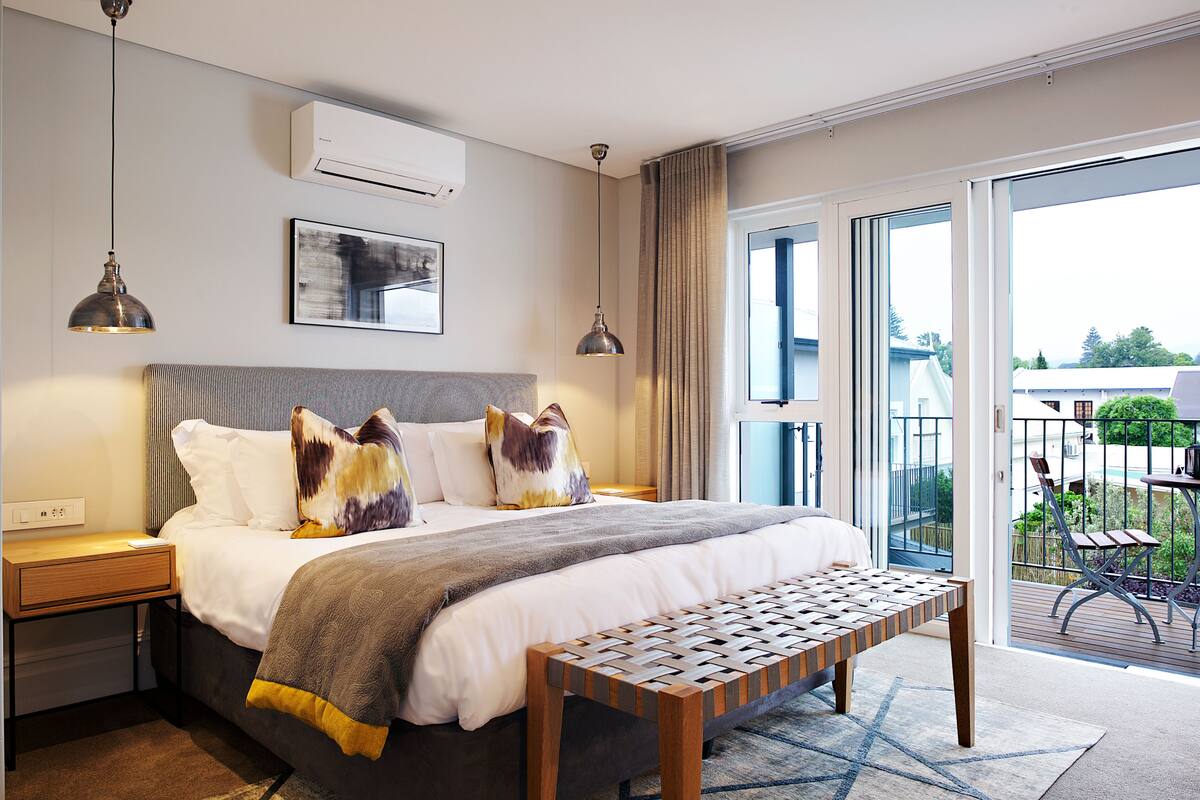 Een moderne hotelkamer met een groot bed, een bankje en een balkon met tuinmeubilair.