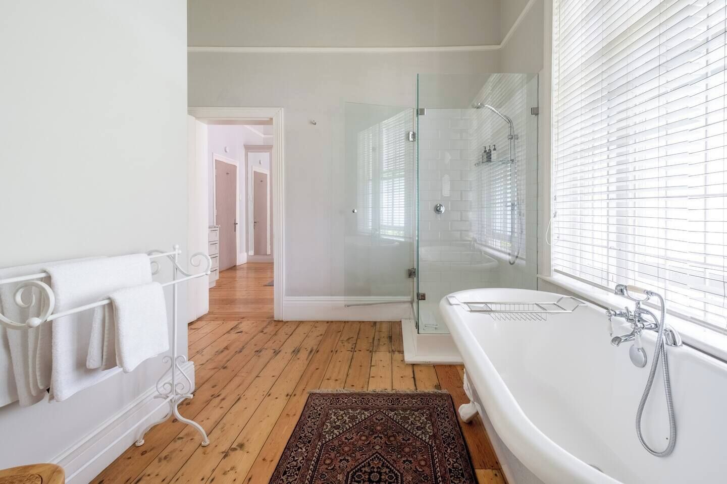 Een moderne badkamer met een douche in een glazen cabine, een witte badkuip en een houten vloer.