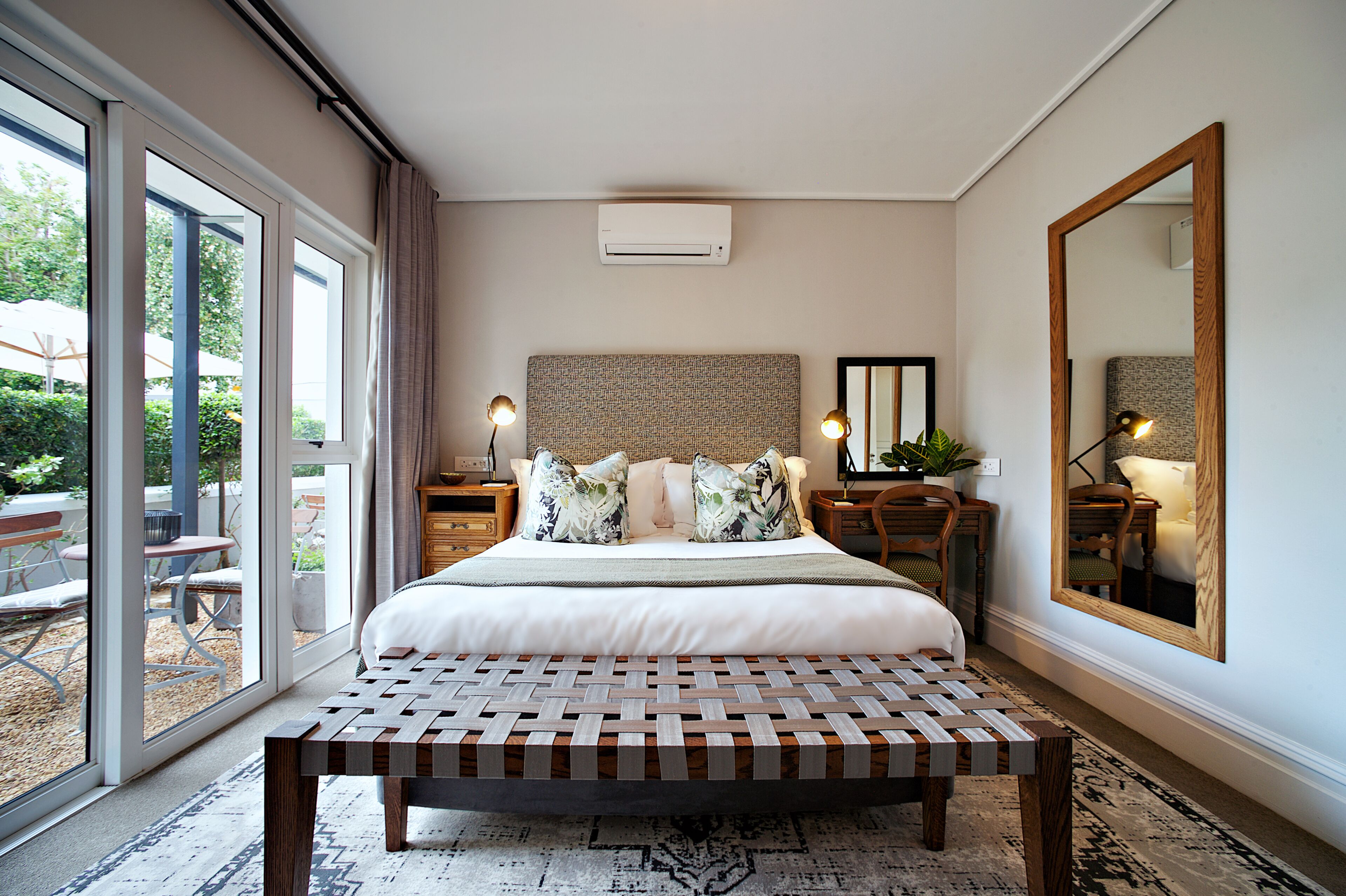 Une chambre avec un grand lit, un banc, un miroir et une vue sur l’extérieur.