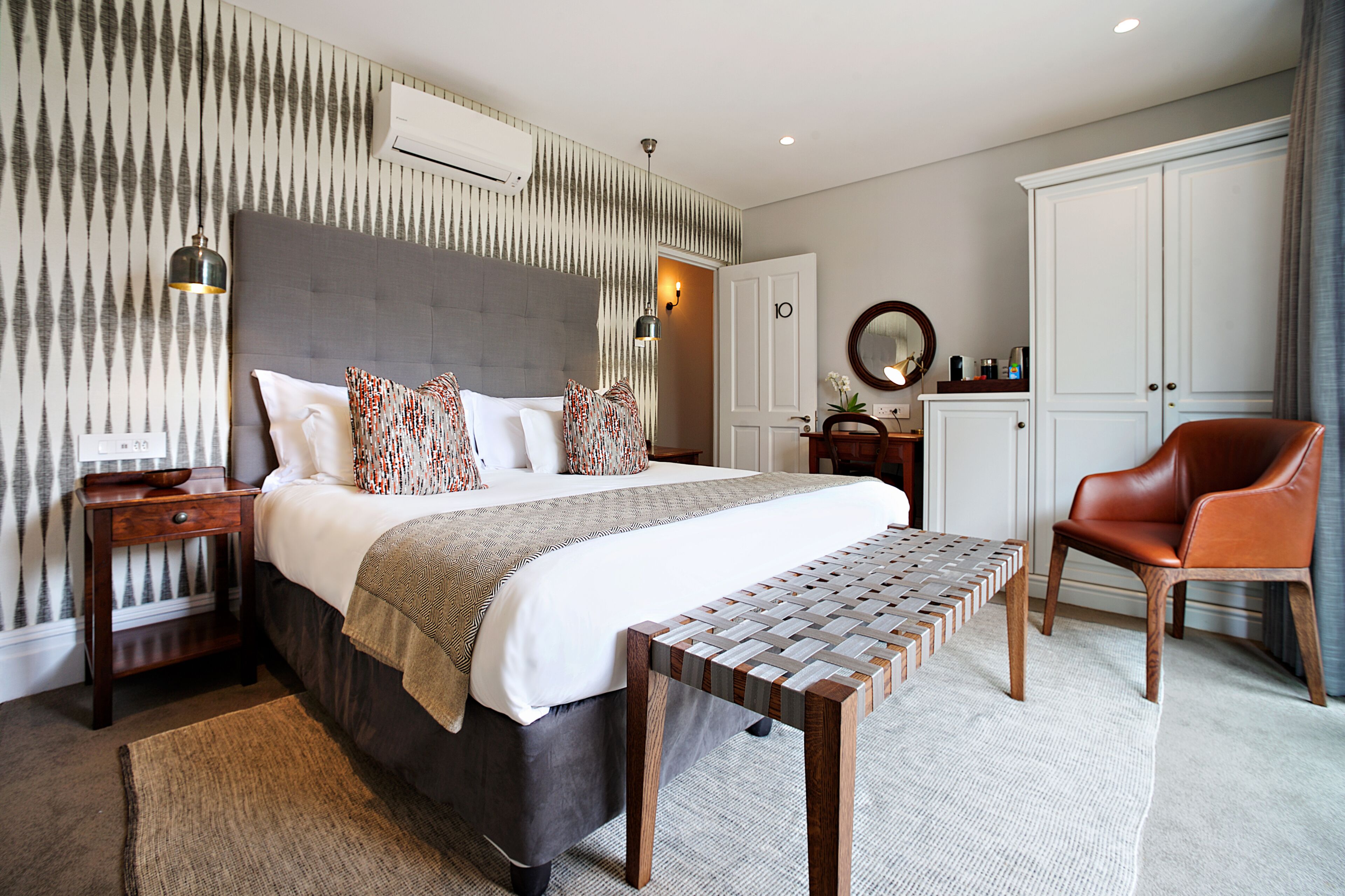 A modern hotel room with a large bed, a wooden bench, a desk, and a wardrobe.