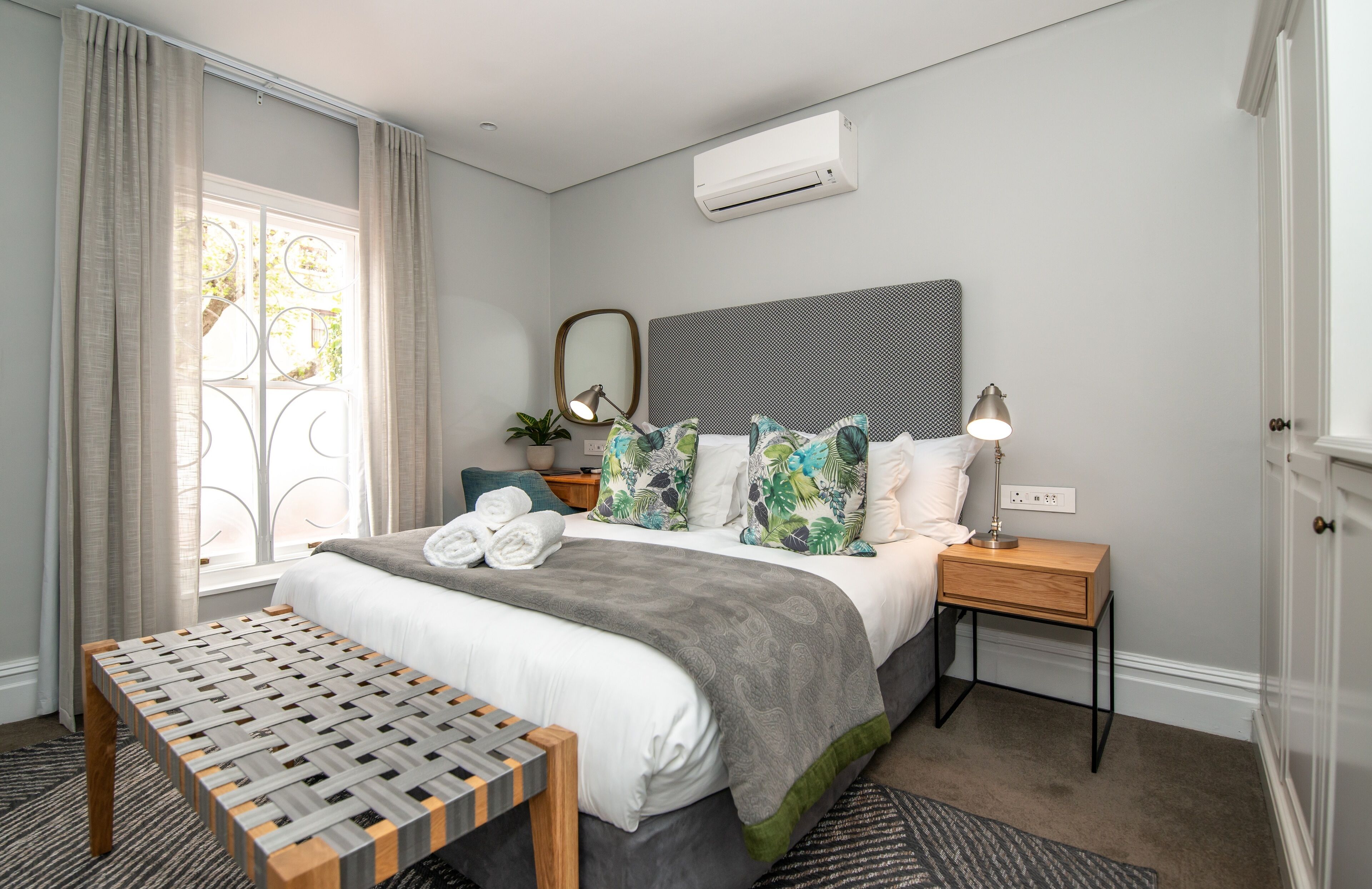 Ein ordentlich eingerichtetes Schlafzimmer mit einem Bett, Nachttischen, einer Bank und einem Fenster mit Vorhängen.