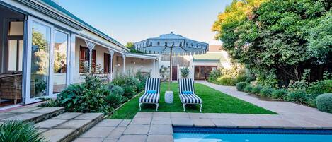 Un patio trasero con piscina, dos sillas de descanso y una sombrilla.