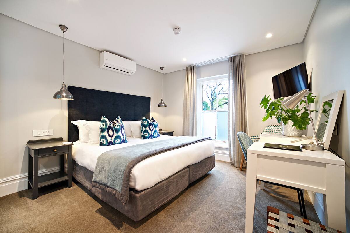 Een moderne slaapkamer met een groot bed, nachtkastjes, een bureau en een raam met gordijnen.