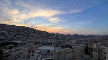 Un paisaje urbano con vistas a una zona densamente poblada, una estructura cúpula destacada y un paisaje montañoso al atardecer.